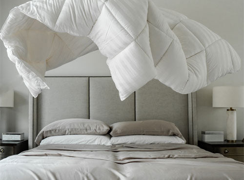 a bed with a duvet being thrown on it