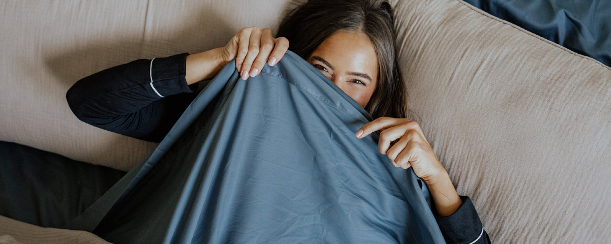 a woman lying in a bed with bamboo sheets, hiding her face behind the top sheet