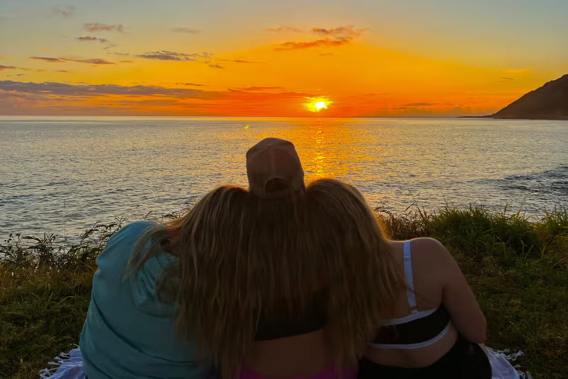 3 women watching a sunset near the ocean