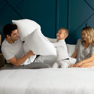 Family having a pillow fight on a bed dressed in white Cariloha bamboo bedding