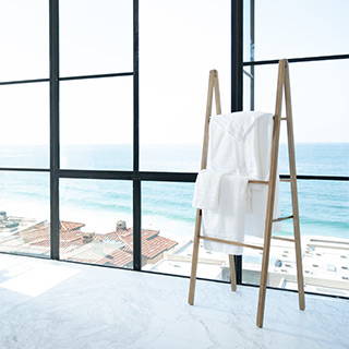 Cariloha bamboo bathrobe and towels hanging on a wooden ladder rack in front of an ocean-view window